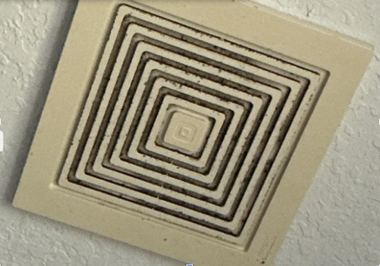 A heavily clogged bathroom exhaust vent fan with visible dust and debris buildup, reducing ventilation and contributing to mold risk
